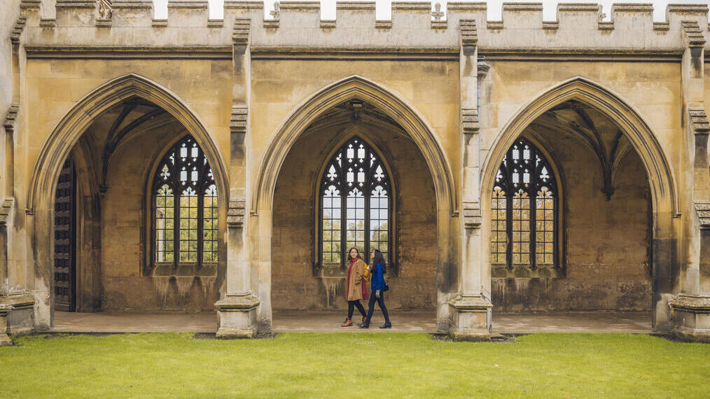 Two women walking under the arches of a college quad