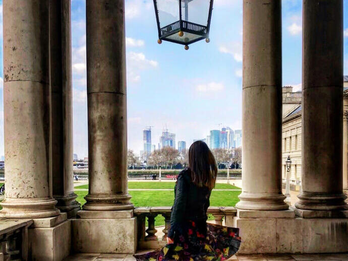 Woman standing underneath a large glass lantern, looking through the colonnades towards modern city buildings
