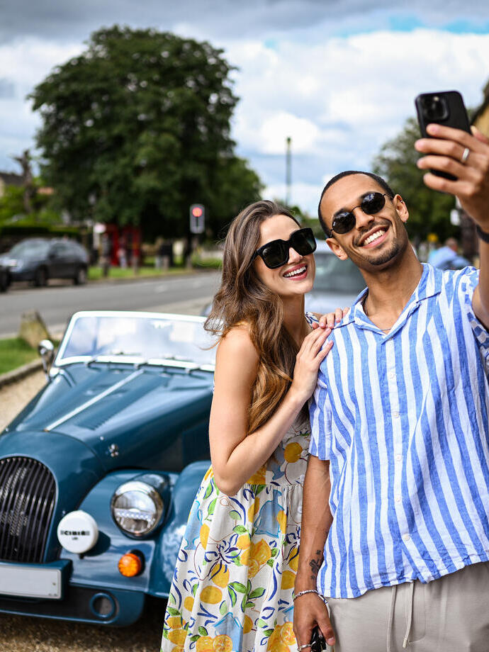 A man and a woman take a selfie in front of a classic car