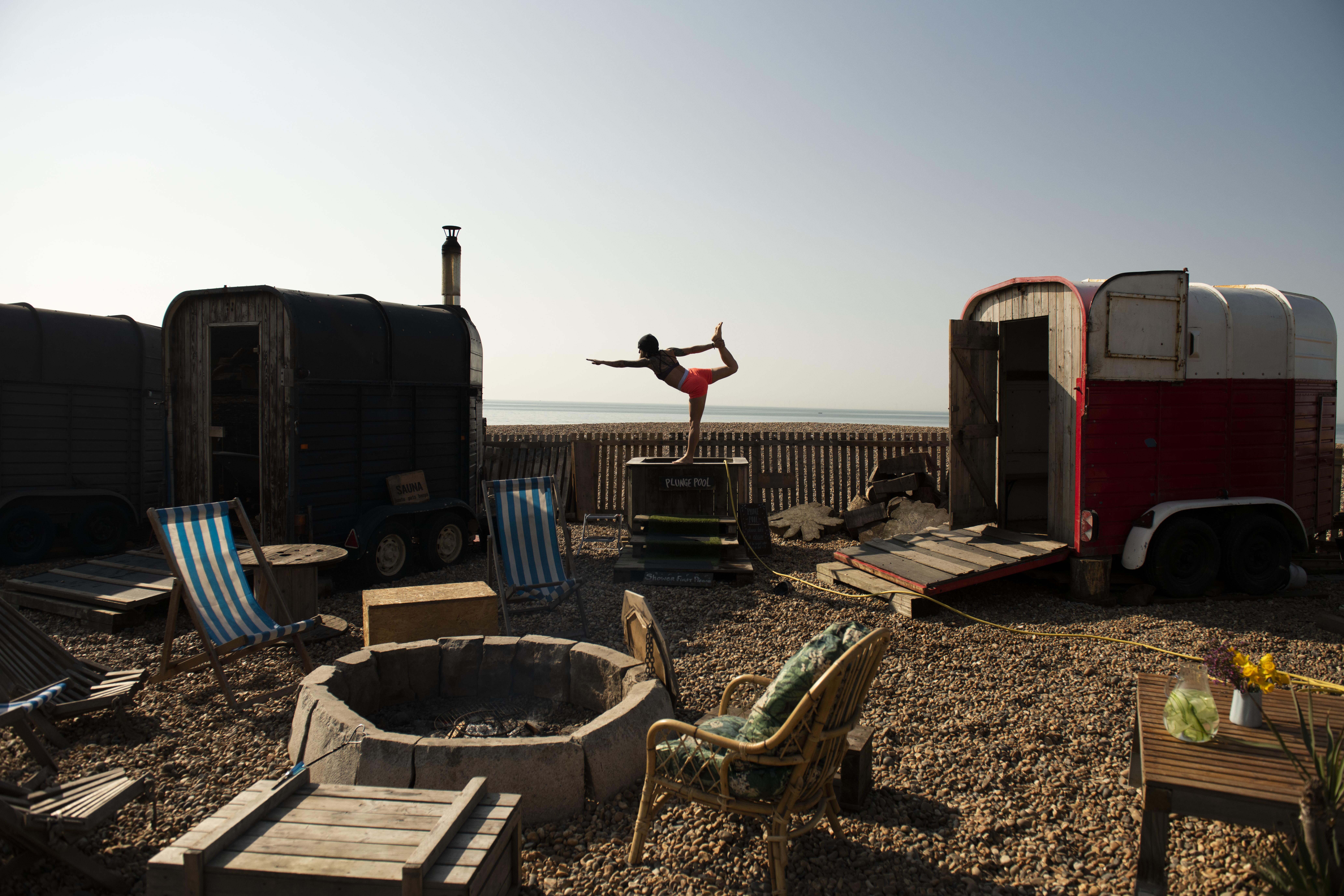 Woman holds a yoga pose standing on the edge of small plunge pool on the beach
