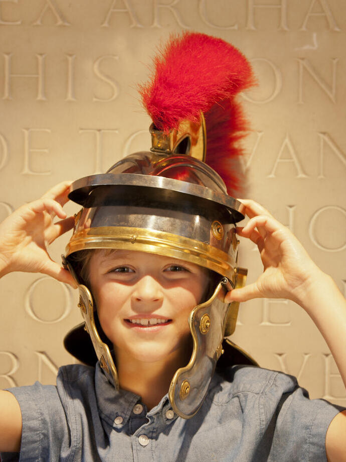 Child wearing a Roman Centurion helmet with a red feather