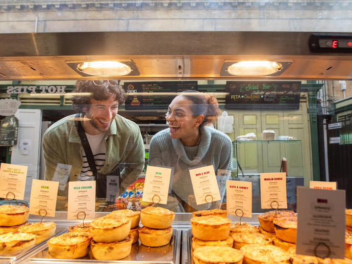 Friends admiring bakery pies through a glass divider.