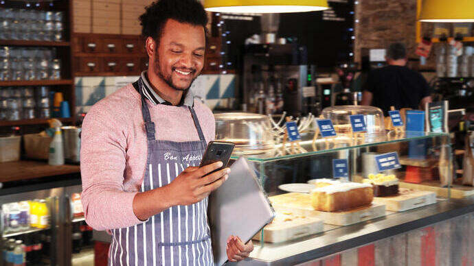 Male cafe owner smiling at his phone in front of the counter in the restaurant