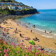 People on a sandy beach in a cove with houses on the cliff behind