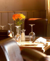 Mesa de restaurante con sillas de cuero, vasos y flores.
