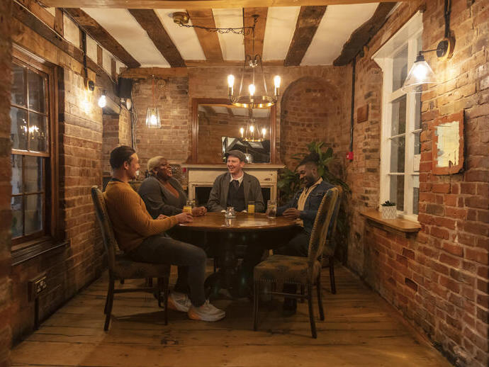 Cuatro personas sentadas alrededor de una mesa redonda en una habitación de ladrillo con luz cálida conversando y riendo.