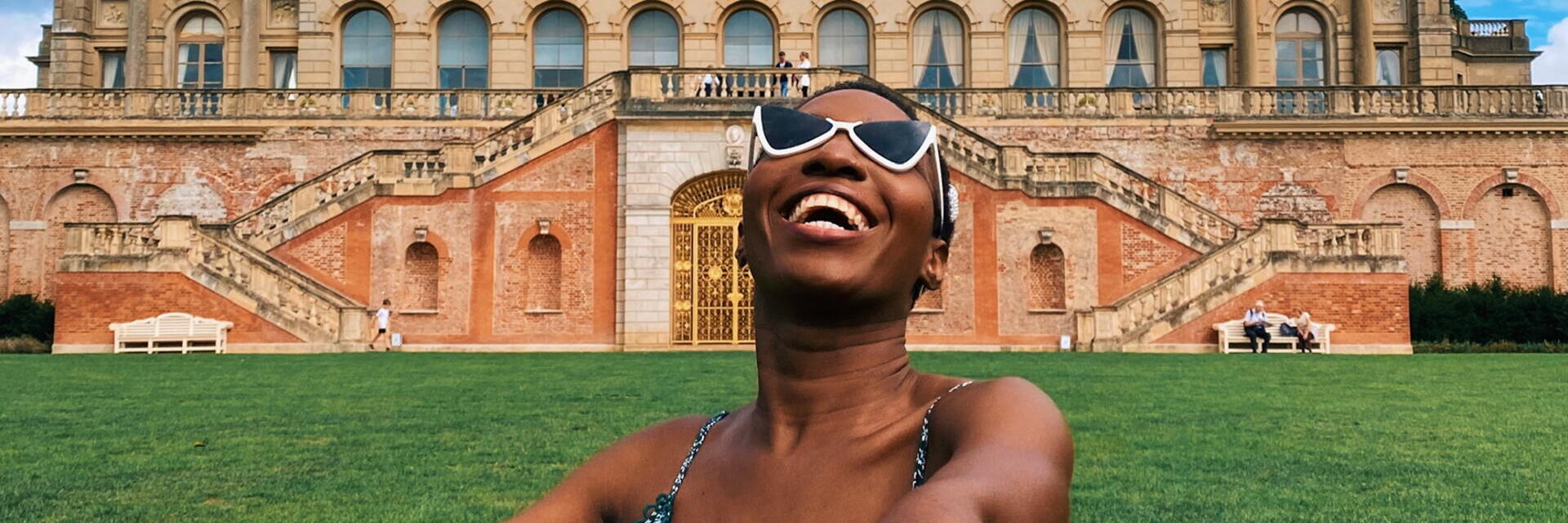 Woman laughing sitting on the grass in front of a stately home