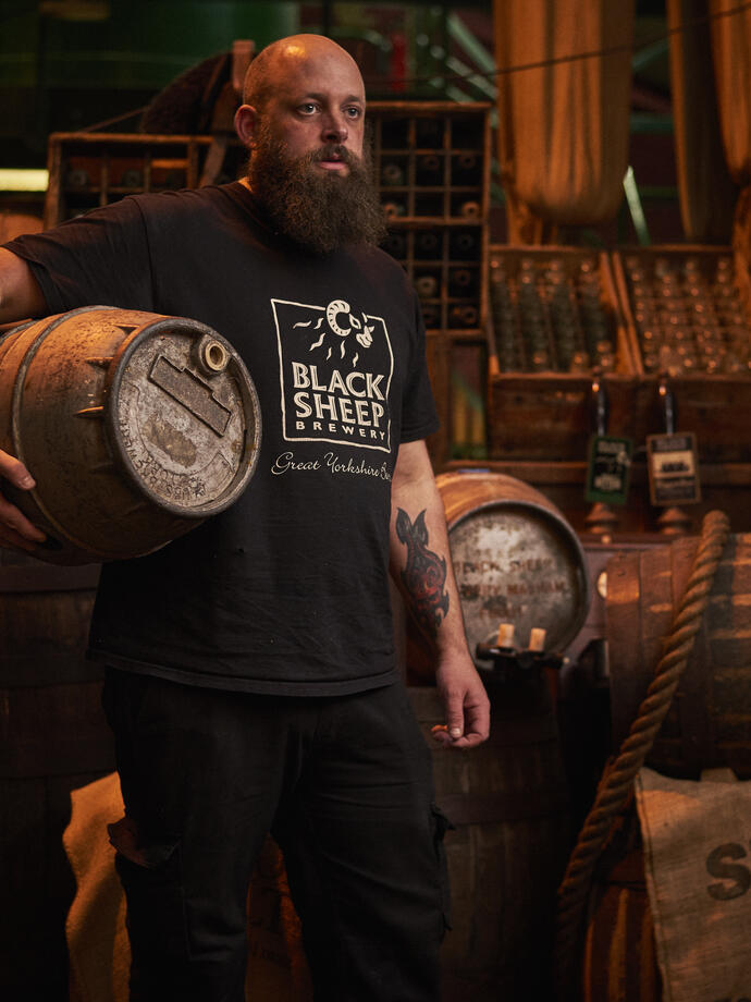 Homme debout dans un entrepôt, tenant un tonneau de bière en bois