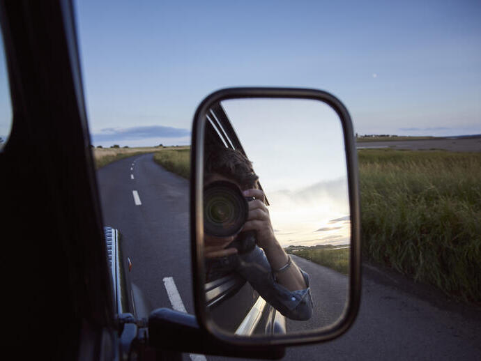 Reflection of a man with a camera in the side mirror of a car