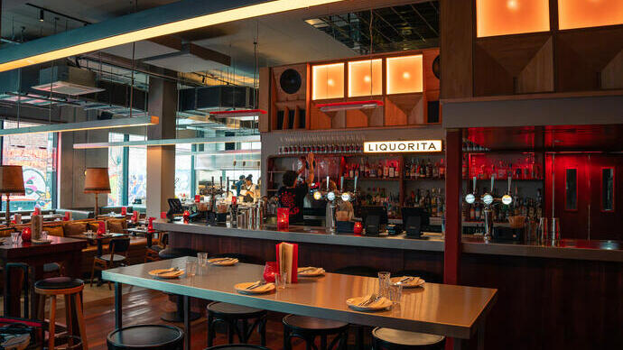 Intérieur de restaurant moderne avec décor en bois, bar, tabourets, tables dressées et éclairage chaleureux.