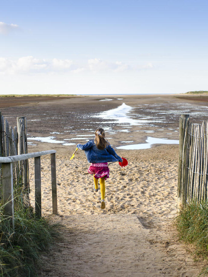 Una niña corriendo por un sendero hacia la playa de Holkham