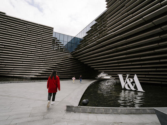 A woman and two girls walking by a modern museum.