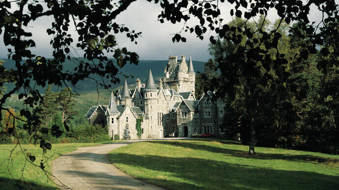 A pathway leading to a fairytale castle, surrounded by manicured lawns and framed by foliage.