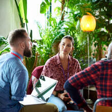 Two men and two women sitting and having a meeting, one of the men is an arm amputee and has a laptop resting on his legs.