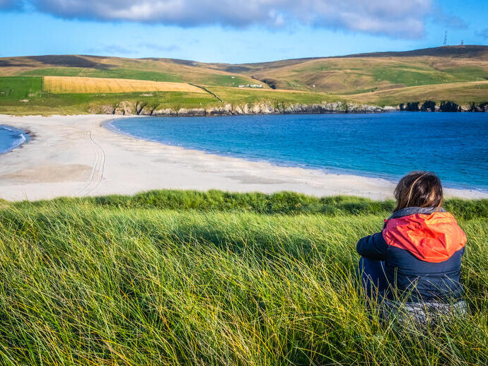 A woman sitting in grass overlooking a spit and fields
