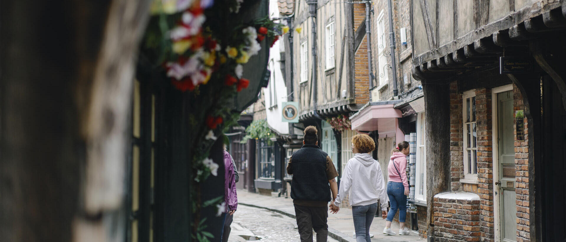 A man and a woman walk down a cobbled street holding hands