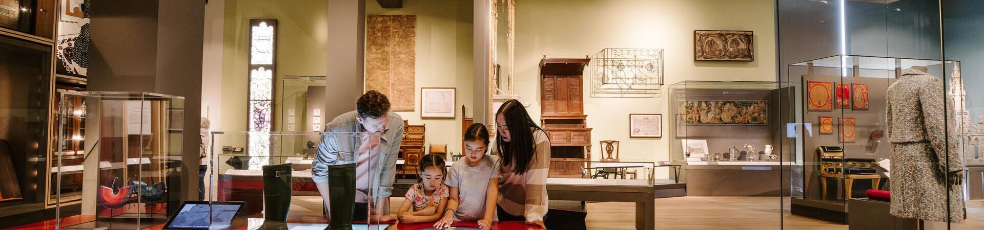 A man, a woman and two girls playing with touch screens inside a modern museum display.