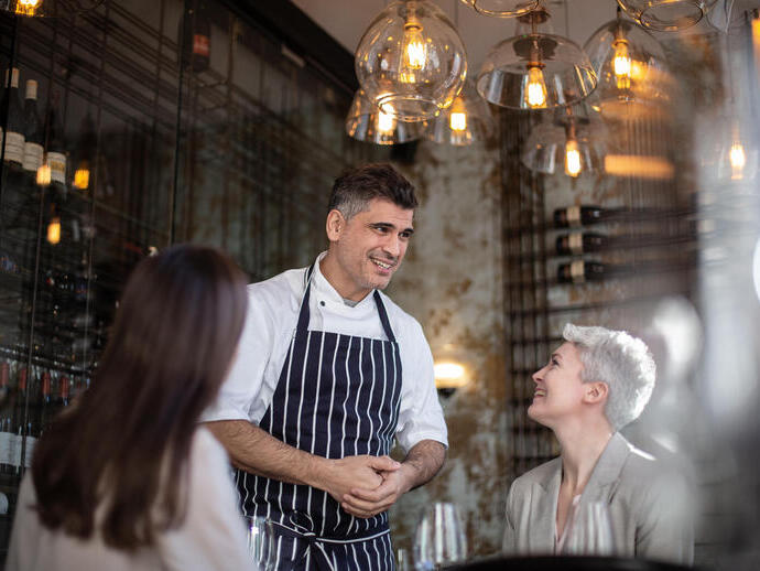 A chef in uniform greeting customers in his restaurant