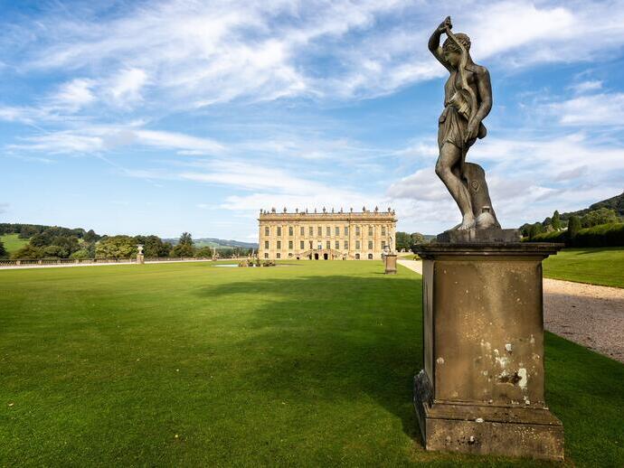 Une statue ornée à l'extérieur d'un magnifique manoir sur une pelouse verte et plate