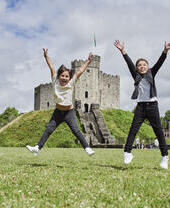 Two children jumping in front of a castle.