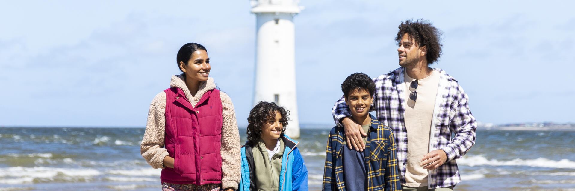 Family walk along a beach with a lighthouse in the background
