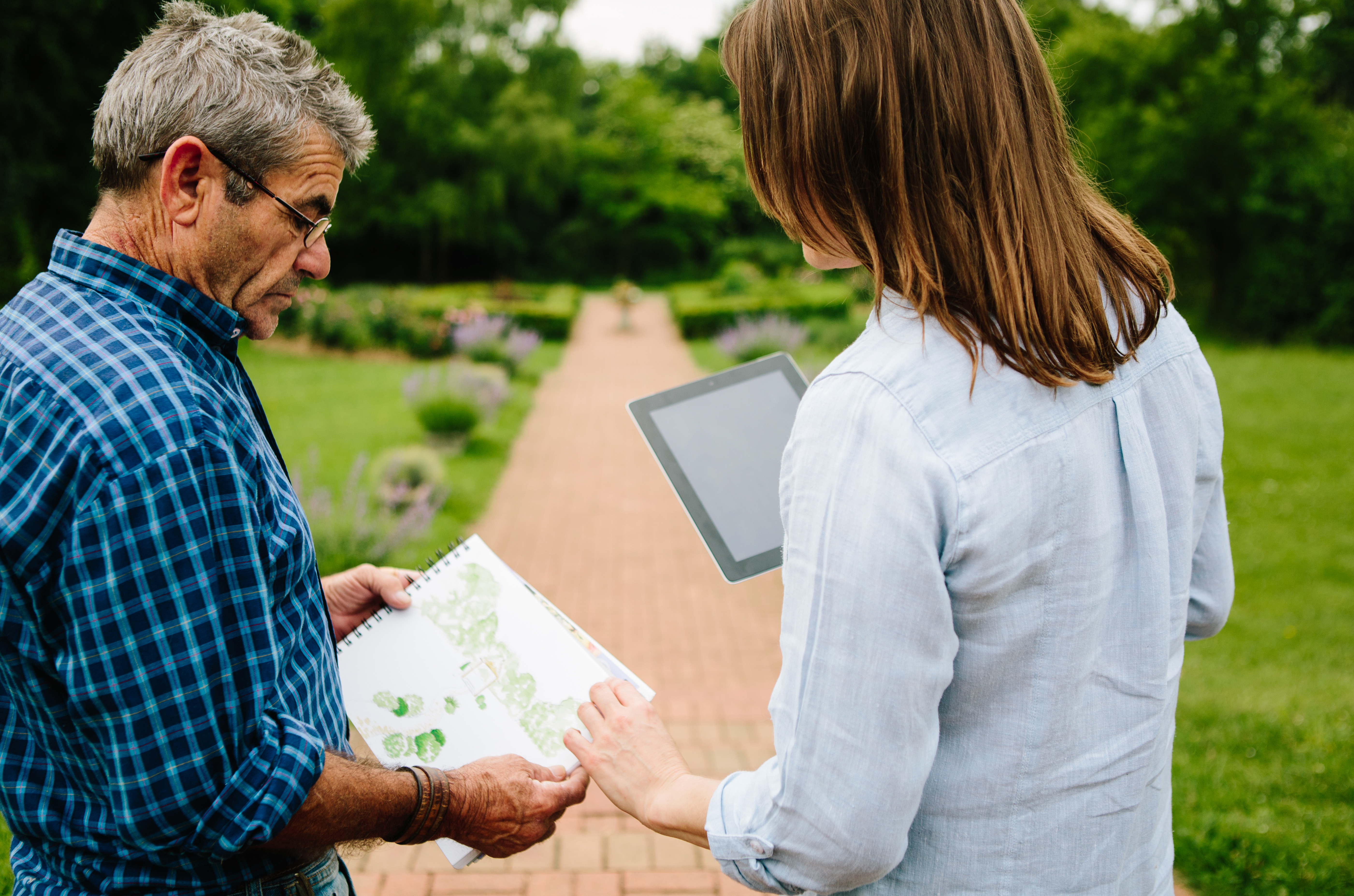 Man and woman sharing garden plans and designs stood on a path in a garden