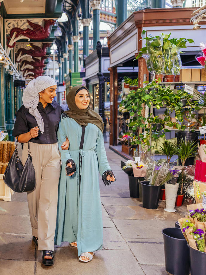 Two women walk past a flower stall in a covered market