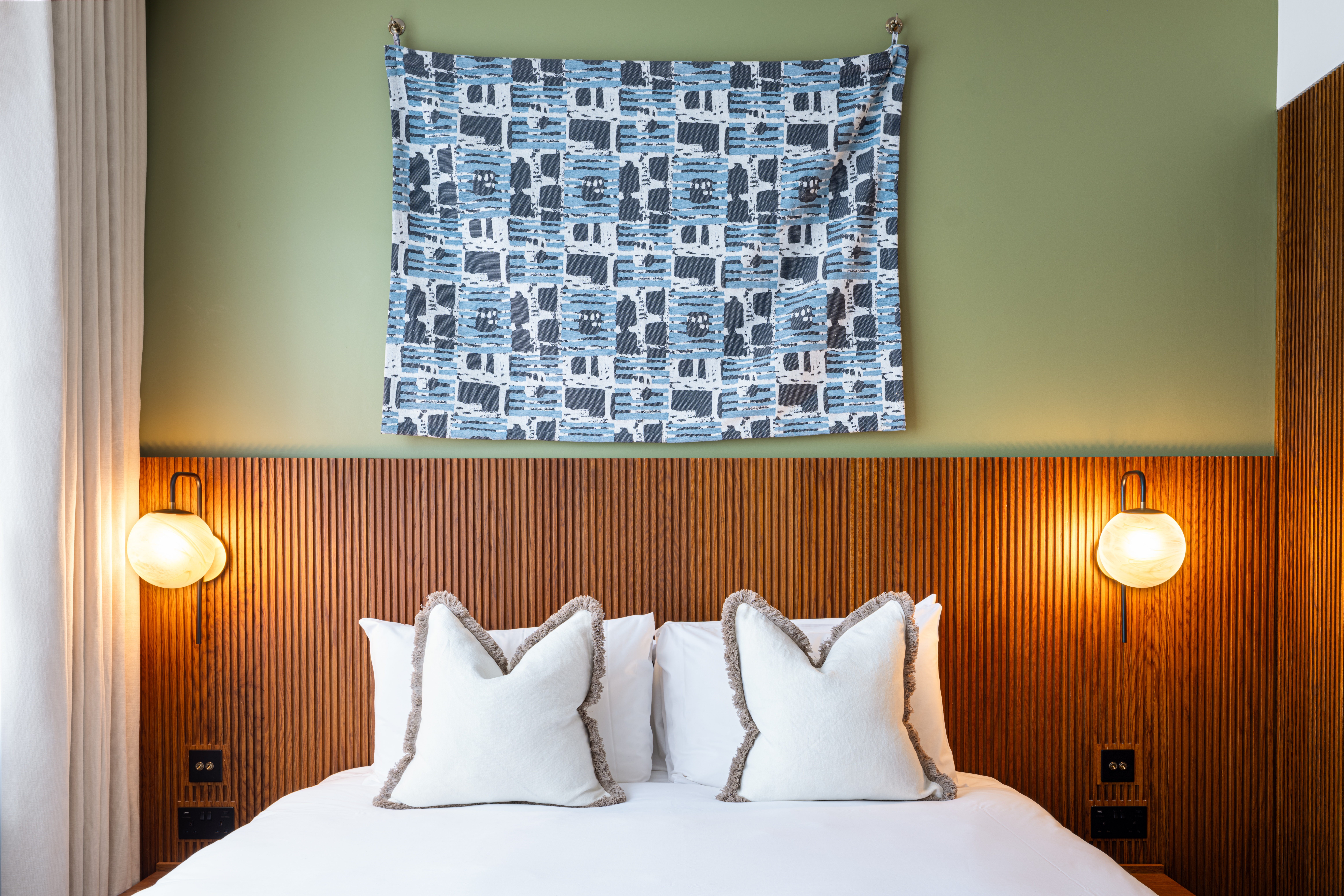 Letto con due cuscini decorativi, applique ai lati e opera appesa alla parete.