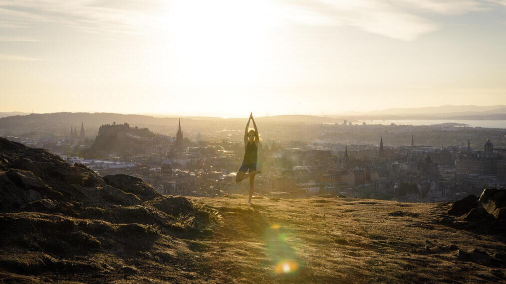 Una joven haciendo yoga en una colina con vistas a la ciudad