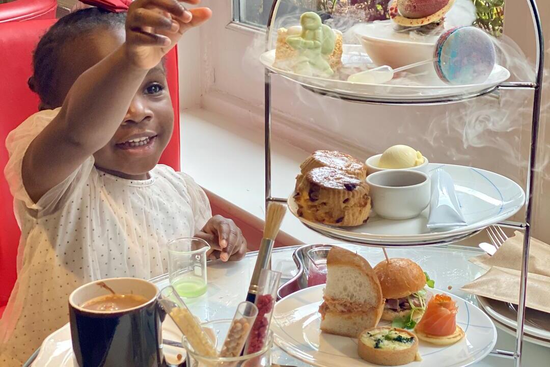 Kind, das bei einem Nachmittagstee in einem Hotelrestaurant nach Kuchen greift