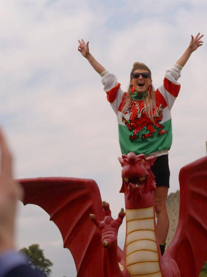 Woman standing with arms outstretched on a model Welsh dragon in front of a castle