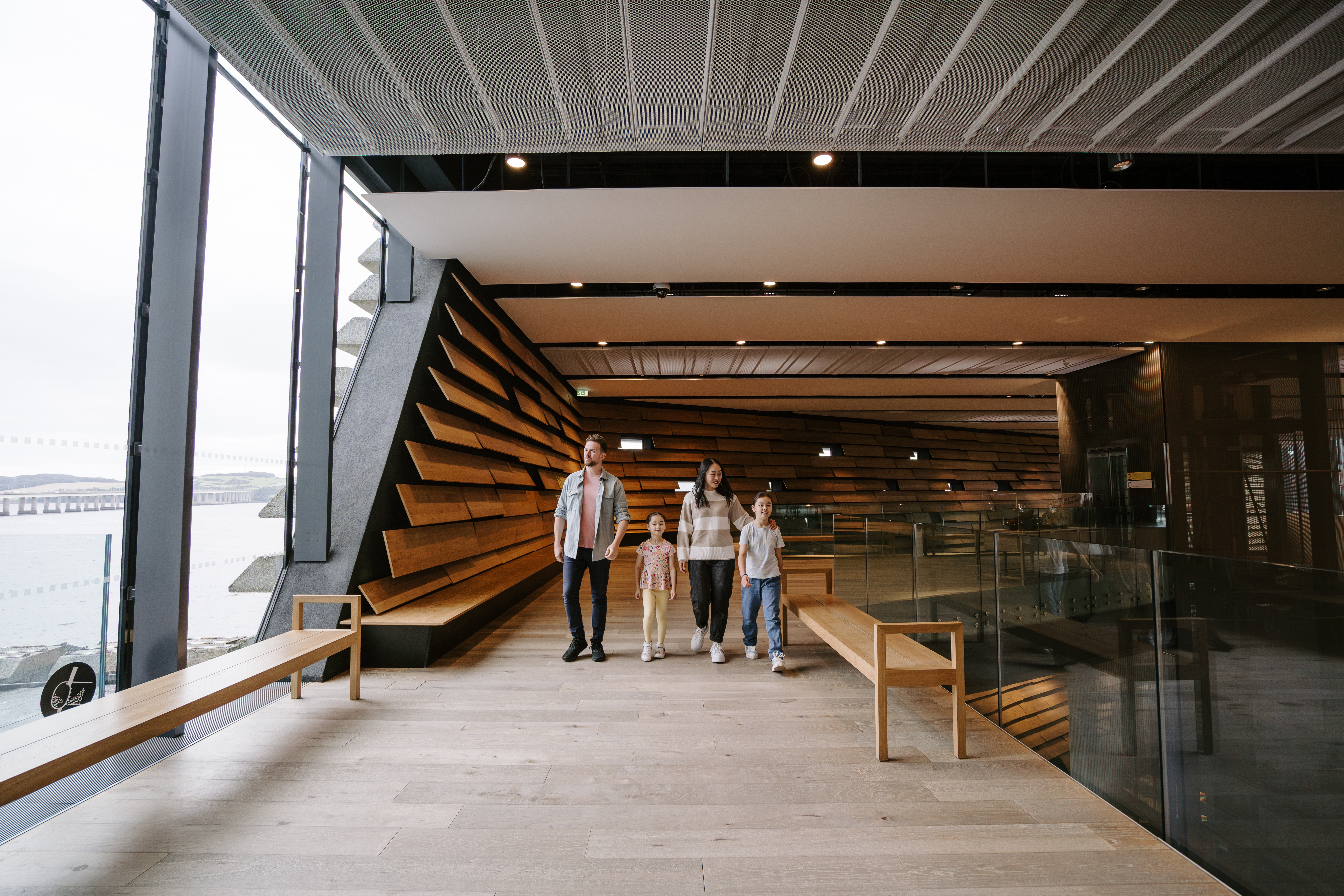 A man, a woman and two girls walking inside a modern museum.