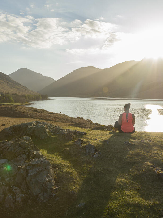 Woman, meditating in green valleys, near lake. The sun is shining.