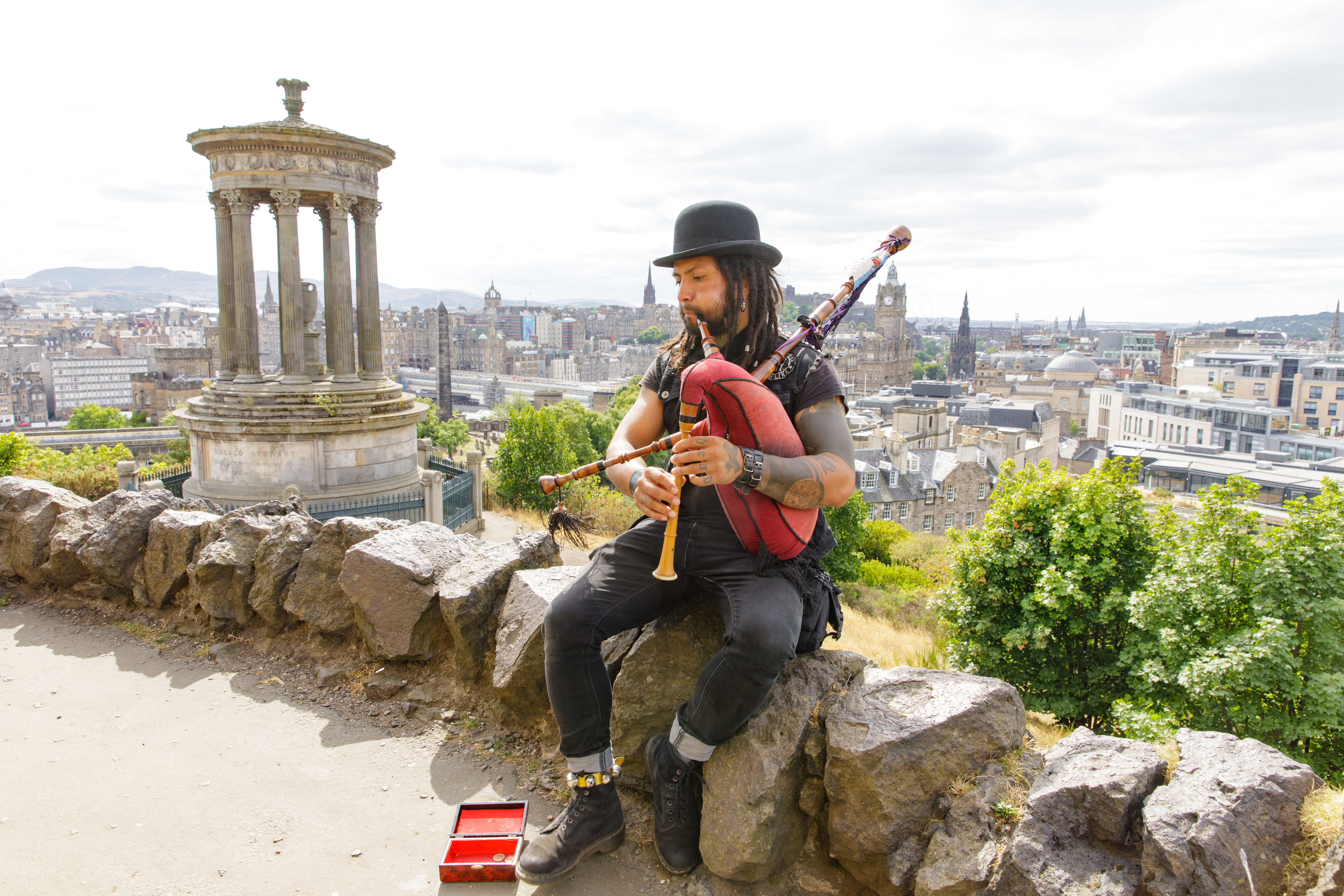 رجل يعزف على المزمار جالسًا على صخرة على تلة تطل على المدينة