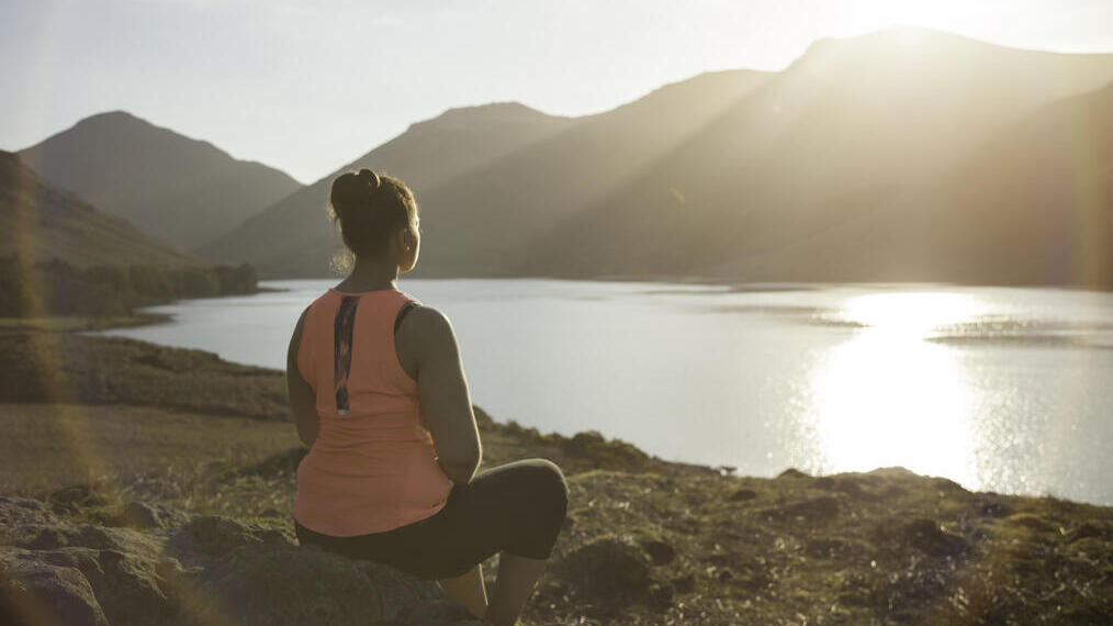 Woman, meditating in green valleys, near lake. High sun