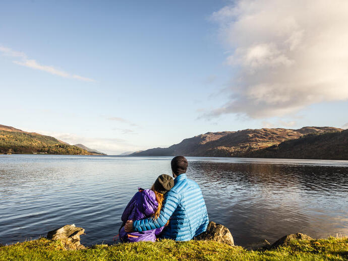 A man and woman sat looking across a lake