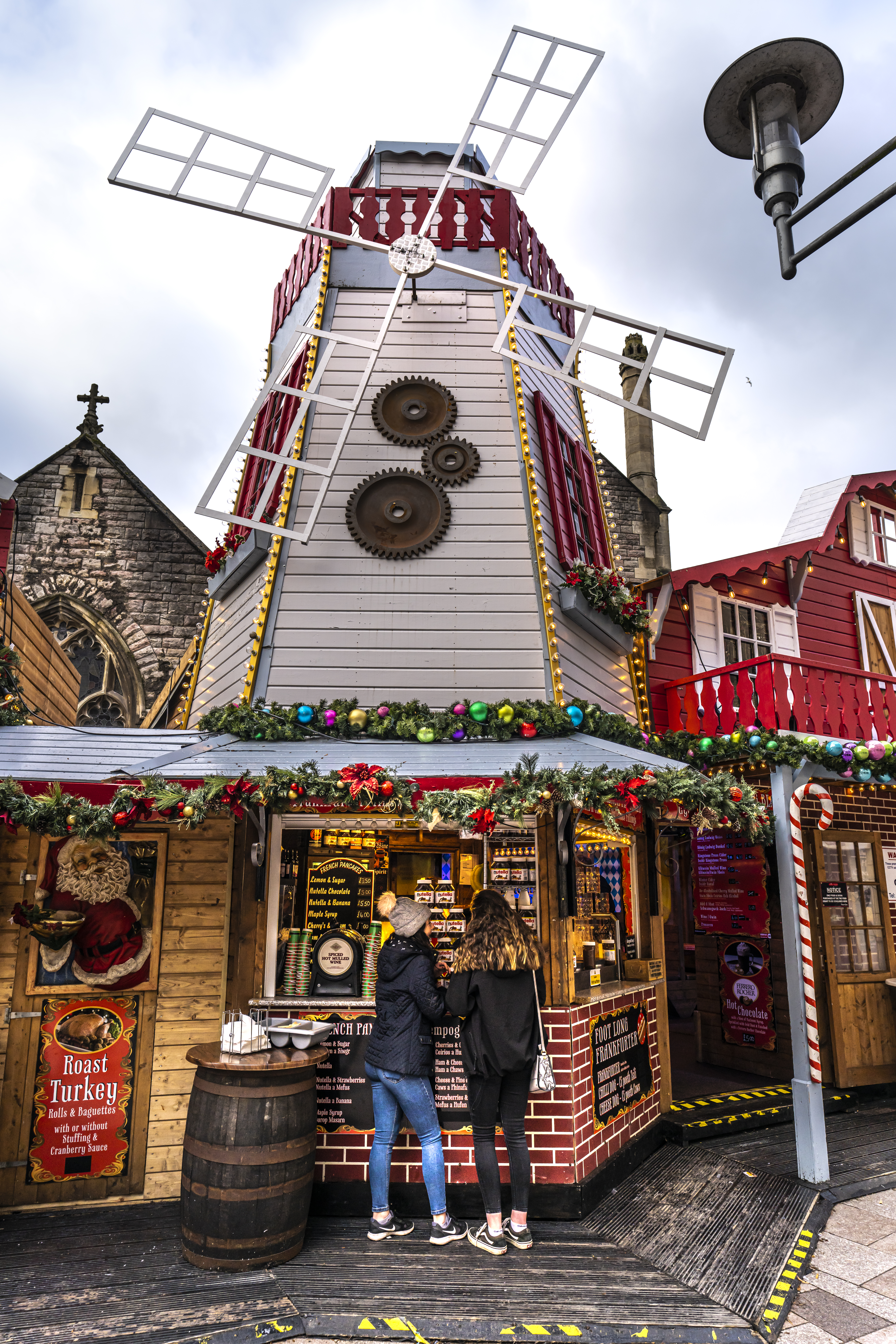 Dos mujeres de pie frente a un puesto de un mercado navideño