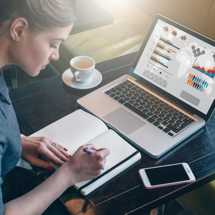 Young business woman sitting at table and taking notes in notebook