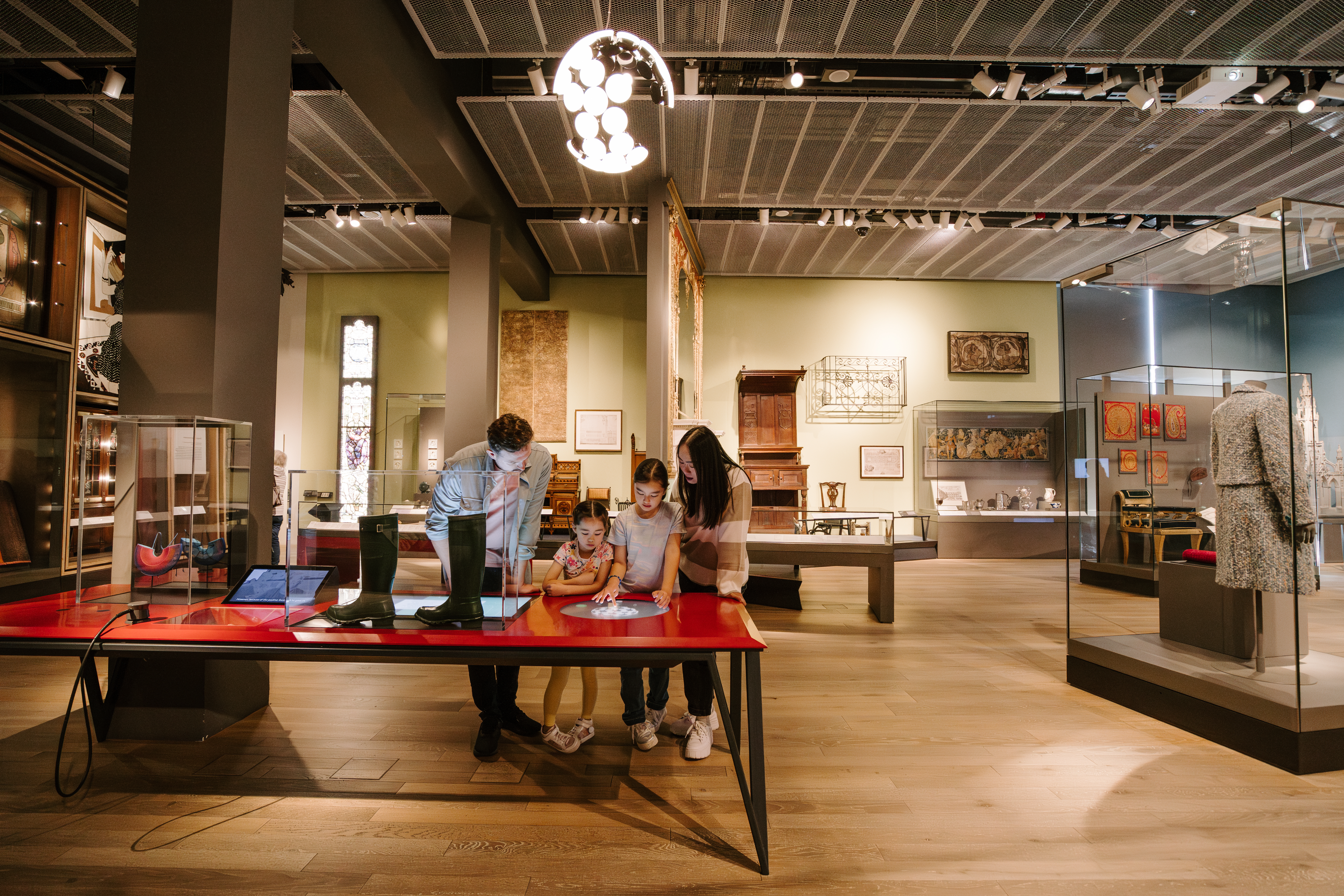 A man, a woman and two girls playing with touch screens inside a modern museum display.