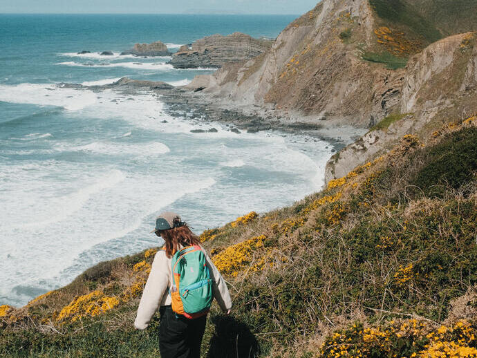 A woman walks along a coastal path with sea and headland in the distance