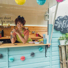 Young woman stood in the hatch of a food truck smiling, ready to serve