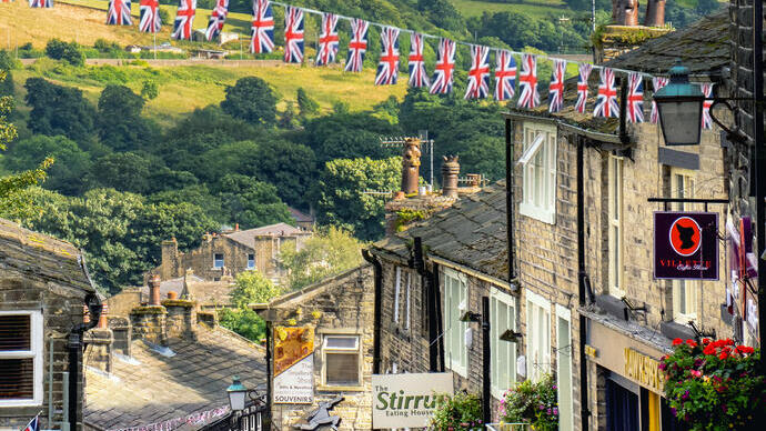 People walking in a steep cobbled village street with Union Jack bunting hanging from the houses