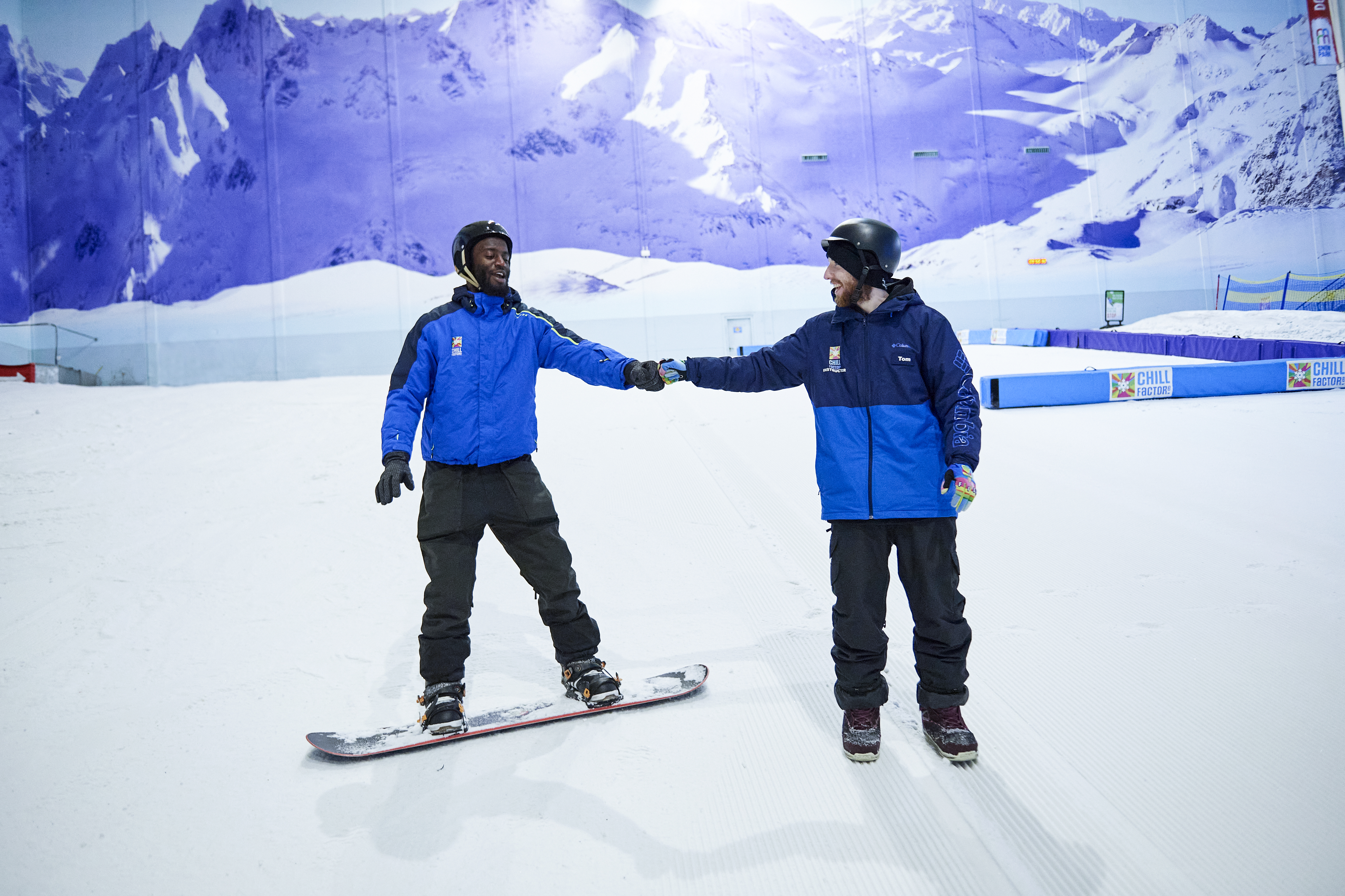 Two men skiing and snowboarding on an indoor snowslope at Chill Factore in Manchester