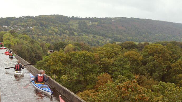 People kayaking across an elevated aqueduct with views of the valley below.