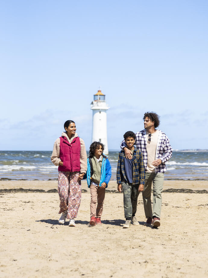 Family walk along a beach with a lighthouse in the background