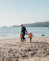 Une famille se promenant sur la plage, l'homme est accompagné de deux jeunes enfants et la femme tient une planche de surf à Saundersfoot Beach