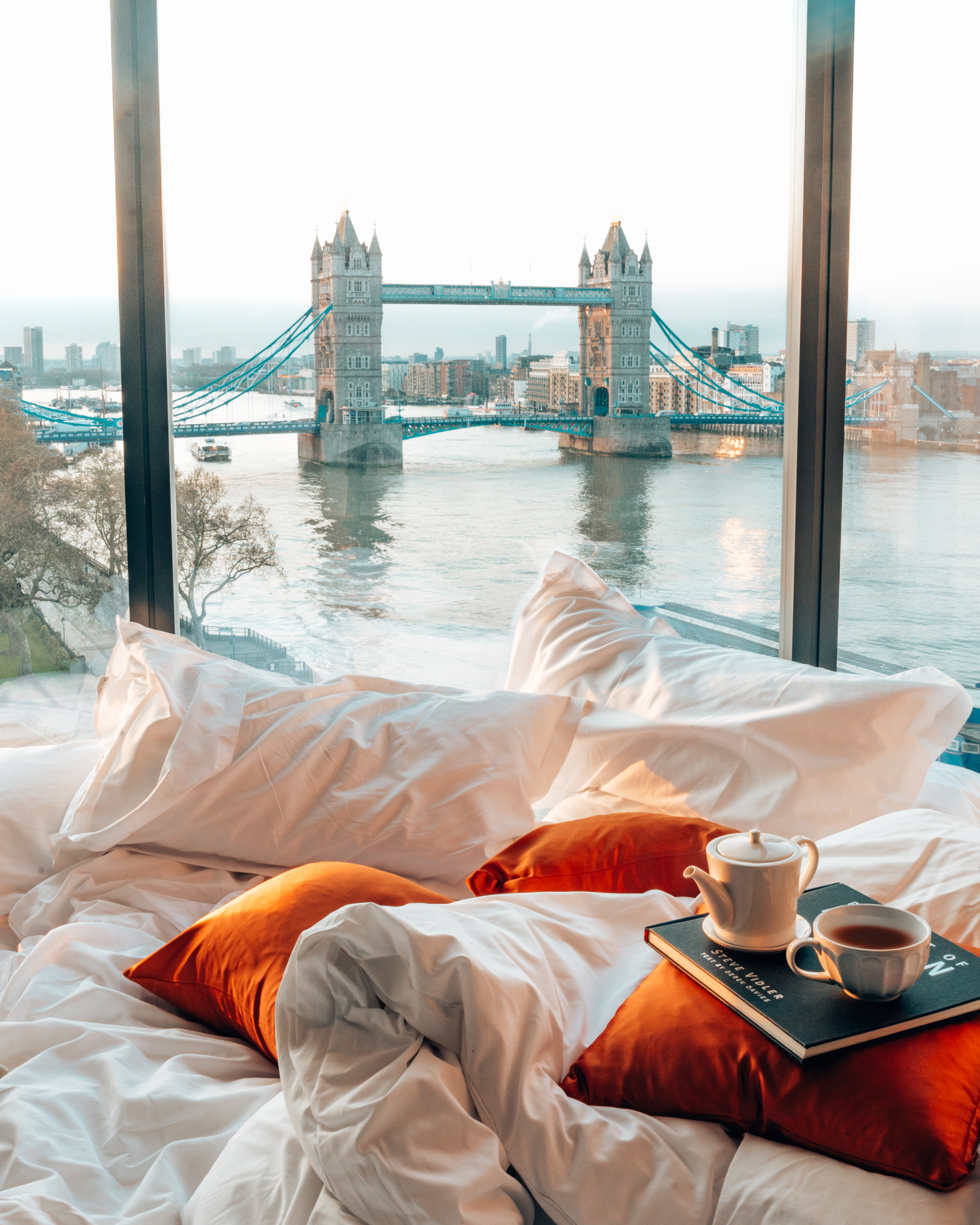 A hotel bedroom with city views of a river and a bridge from the window