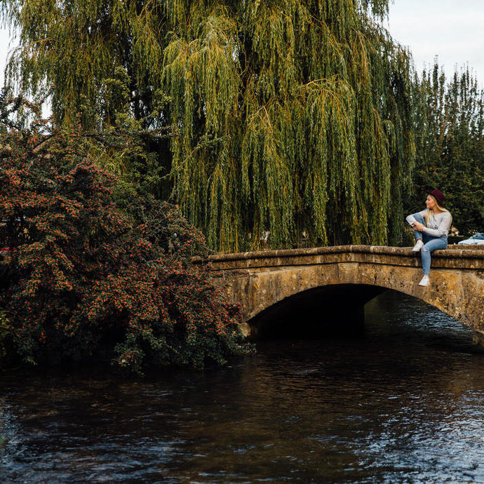 Woman sitting on a low stone bridge over a river in a village