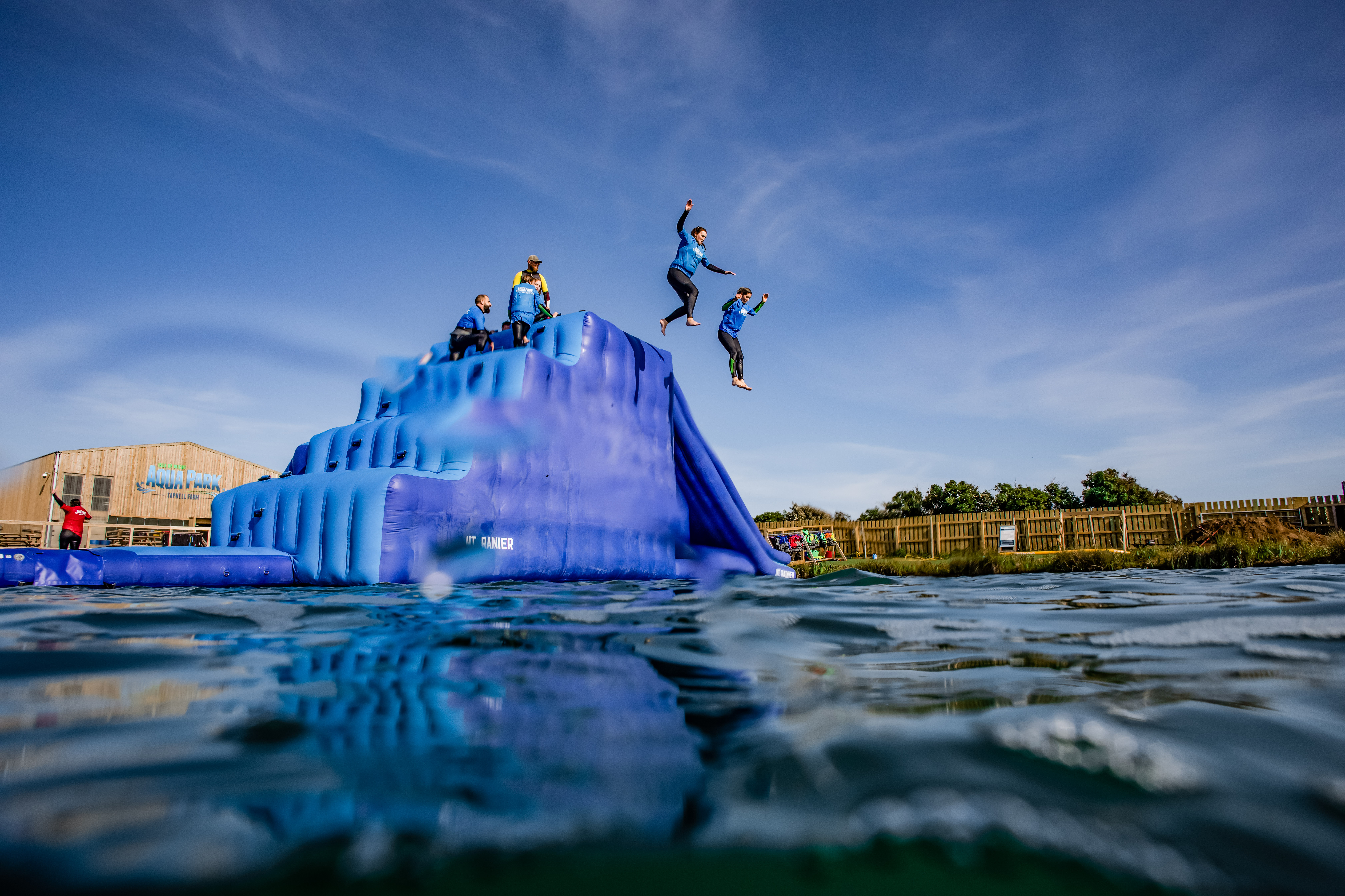 Two women jump from an inflatable obstacle into a lake