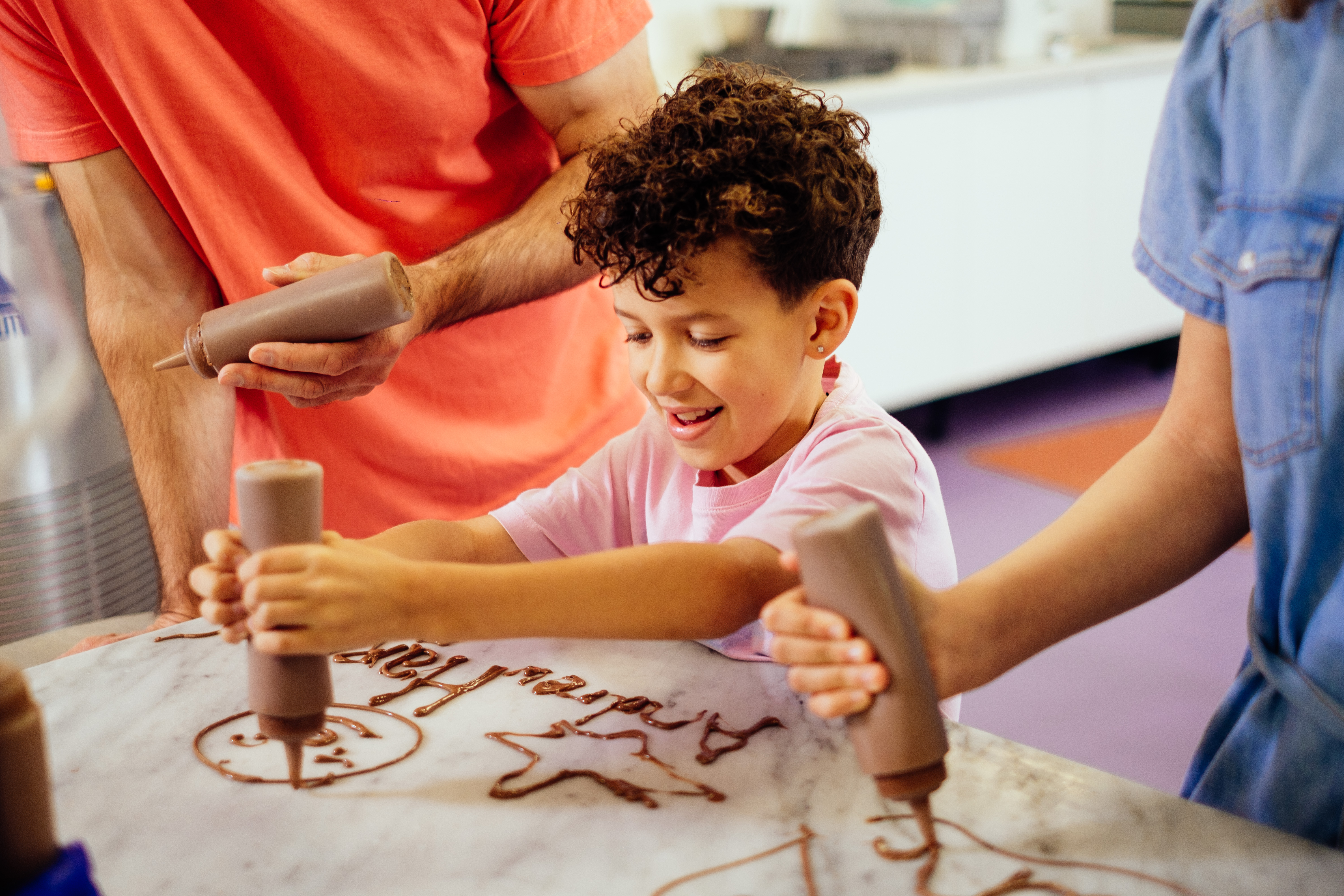 A boy, with curly hair, squeezing chocolate out of a bottle